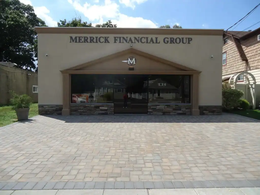 A one-story building with a sign reading “MERRICK FINANCIAL GROUP” above the entrance, featuring large front windows, light-colored walls, and a paved stone driveway in front—ideal for those seeking home improvements in Nassau County, NY.