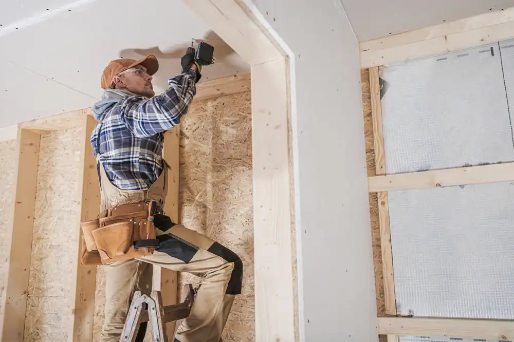 A construction worker uses a power drill on a ladder to install drywall on the ceiling in Nassau County.