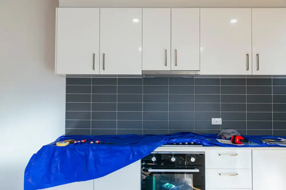 Modern NY kitchen with white cabinets, gray backsplash, blue accents, and Home Improvements Nassau County tools.